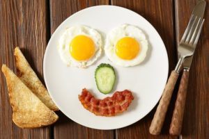 a plate of food placed into a smiley face. Bacon, cucumber, fried eggs, toast