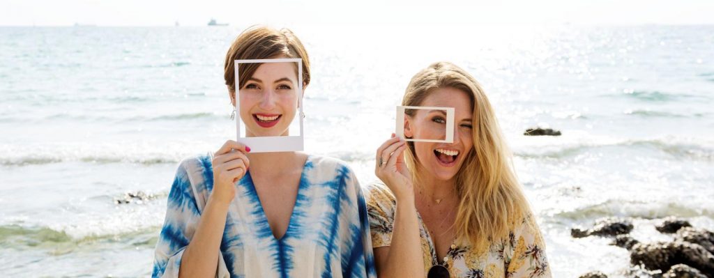 image of 2 women at the beach holding frames around their faces and smiling