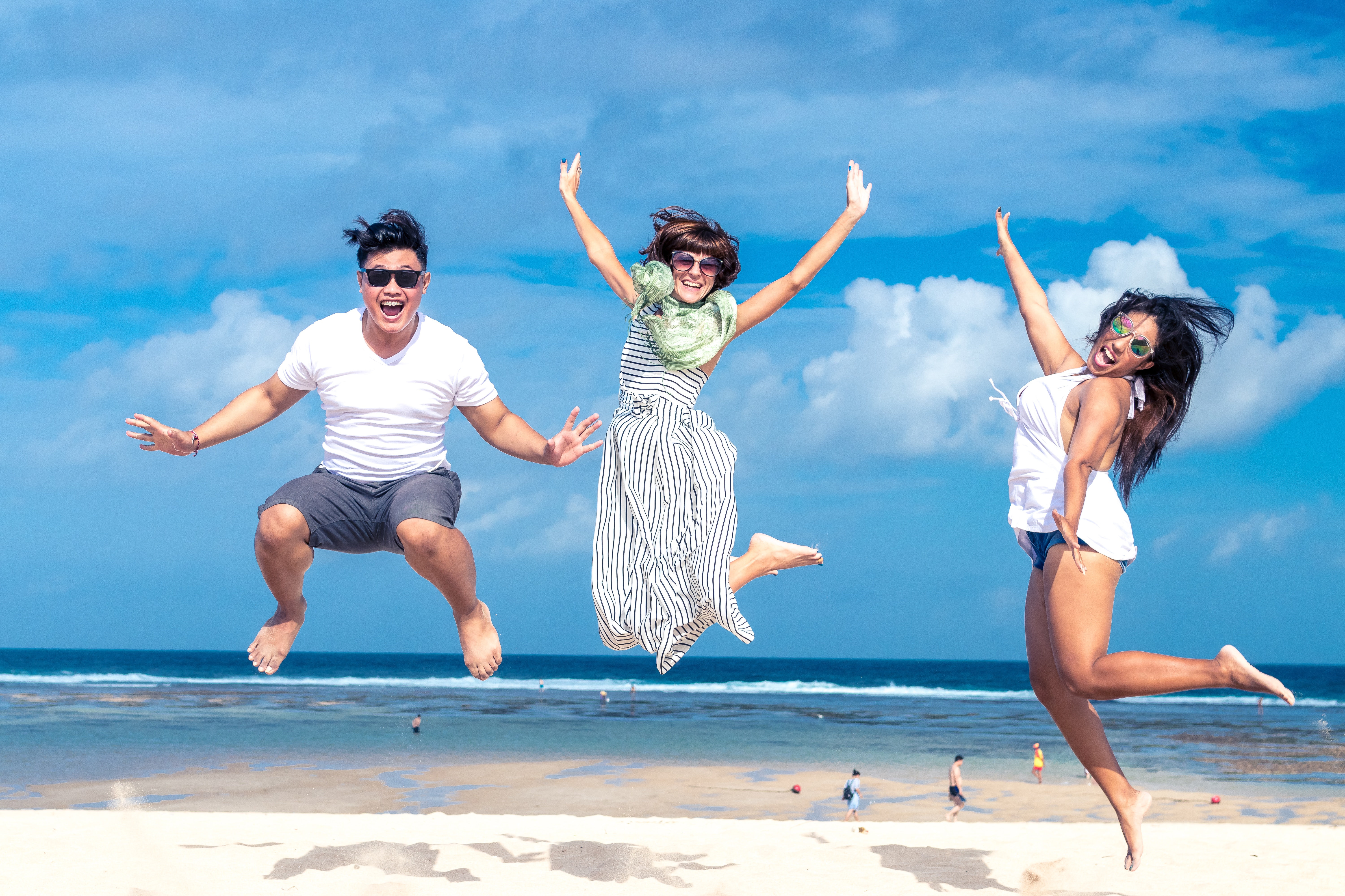 3 people wearing sunglasses and very happy whilst jumping on the sand at the beach