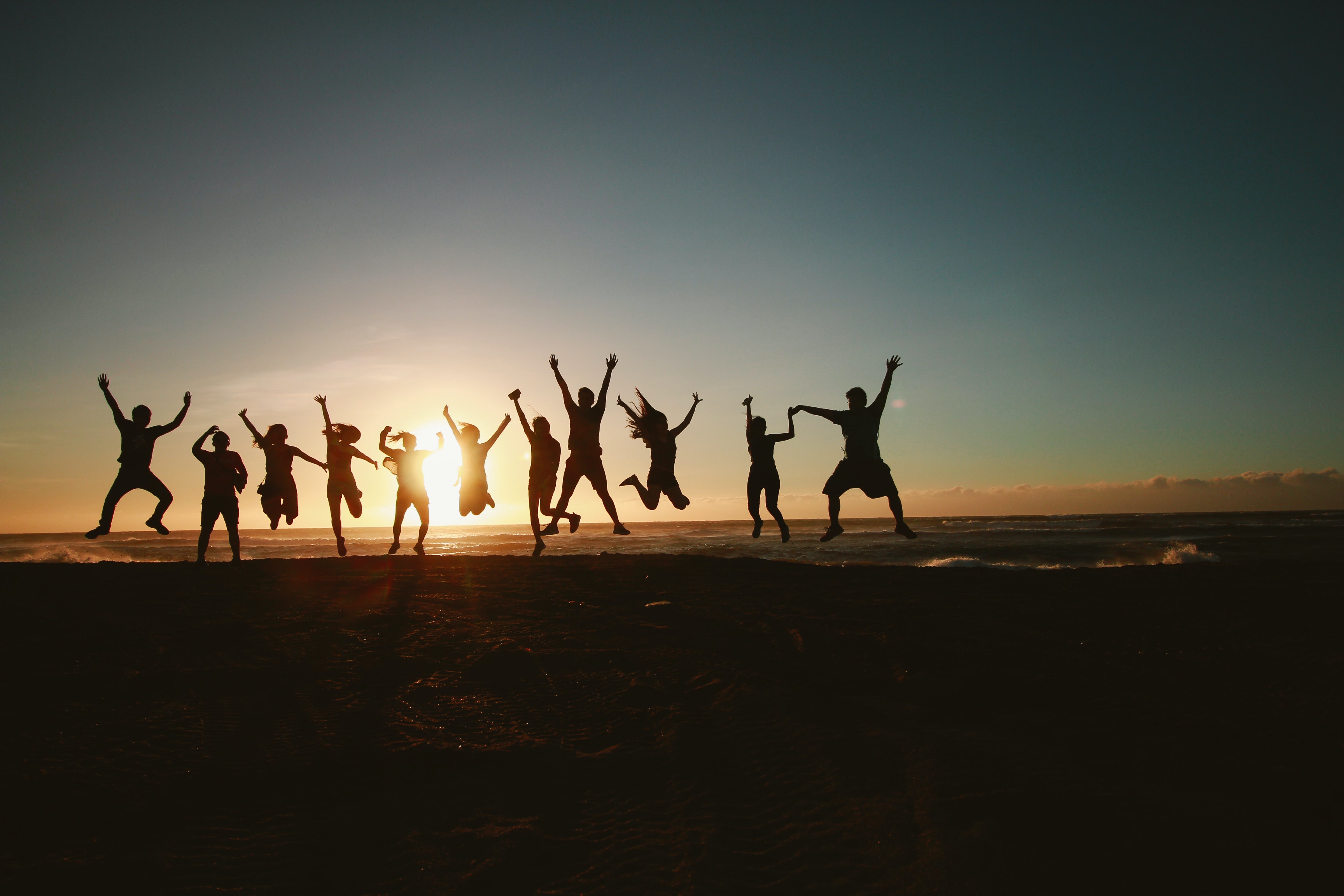 outline of lots of people jumping at sunset at the beach