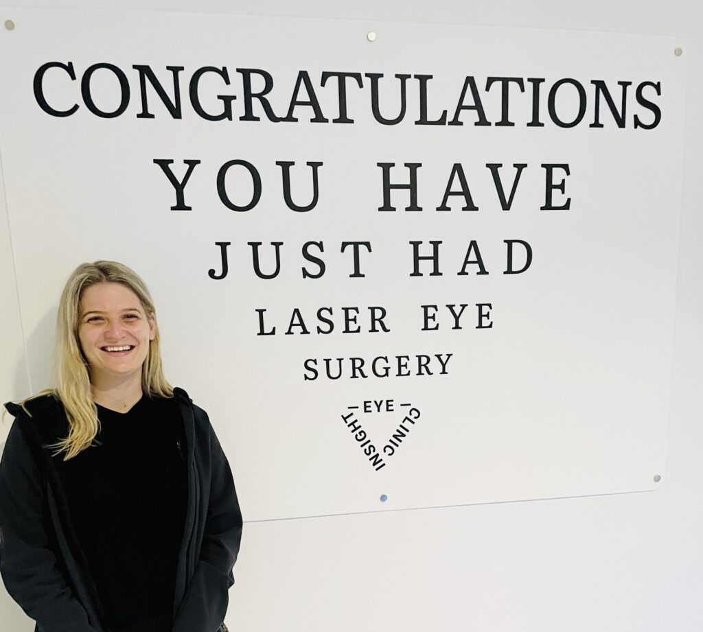Image of patient immediately after laser eye surgery in front of a sign that says 'Congratulations, you have just had laser eye surgery'