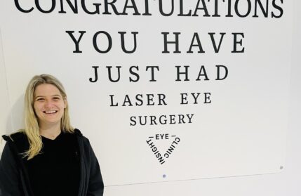 Image of patient immediately after laser eye surgery in front of a sign that says 'Congratulations, you have just had laser eye surgery'
